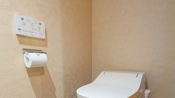 A modern bathroom with a toilet, a wall-mounted flush control panel, and a toilet paper holder.