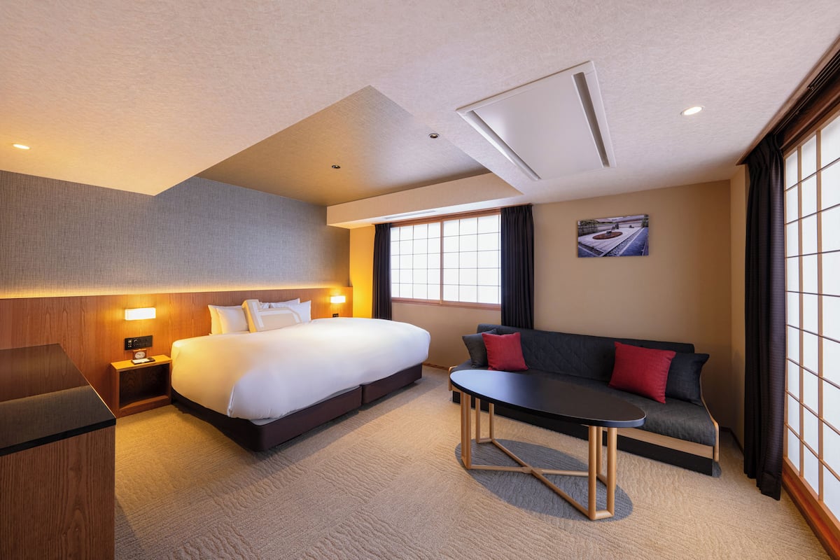 A hotel room with a large bed, a sofa, a small table, and a desk.