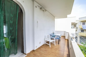 Un balcón con mesa y sillas, una cortina verde y una pared blanca.