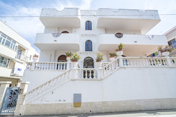 A white building with a central staircase, multiple balconies, and potted plants. - Appartamenti Albero di Giada (Polignano a Mare)