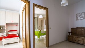 A room with a bed, a wooden bench, a dining table with chairs, and a mirror. - Appartamenti Albero di Giada (Polignano a Mare)