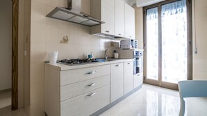 A modern kitchen with a gas stove, microwave, and built-in oven. There is a window with a view of buildings outside. - Appartamenti Albero di Giada (Polignano a Mare)