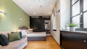 Una habitación de hotel moderna con un sofá, una cama, un mueble de madera oscura y una planta en maceta.