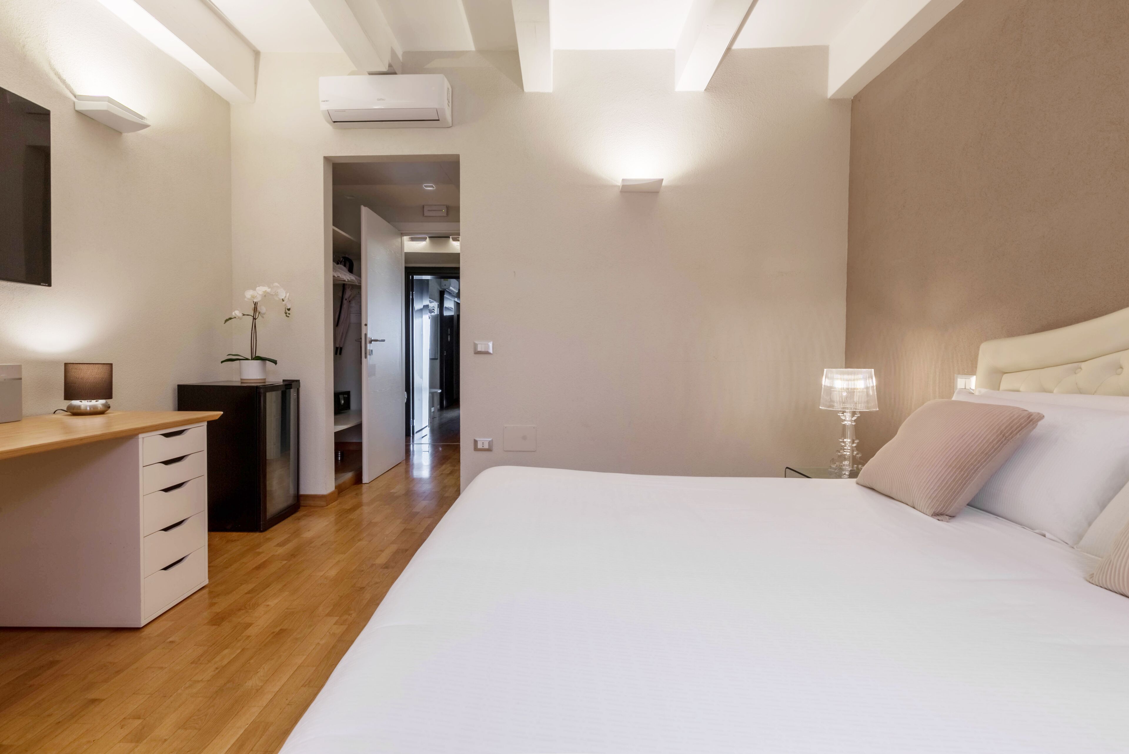 Una camera da letto con un grande letto, un comodino, una scrivania e una sedia. Si apre una porta verso un'altra stanza.