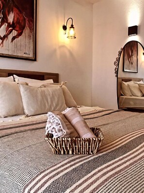 A bedroom with a bed, pillows, a decorative basket, a wall-mounted light, and a painting. - Alacati Umitev Hotel (Cesme)
