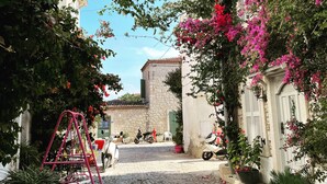 A cobblestone street with a swing set, parked scooters, and a stone building with shutters. - Alacati Umitev Hotel (Cesme)