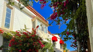 A cobblestone courtyard with blue chairs and a table, surrounded by buildings with red awnings and flowering plants. - Alacati Umitev Hotel (Cesme)