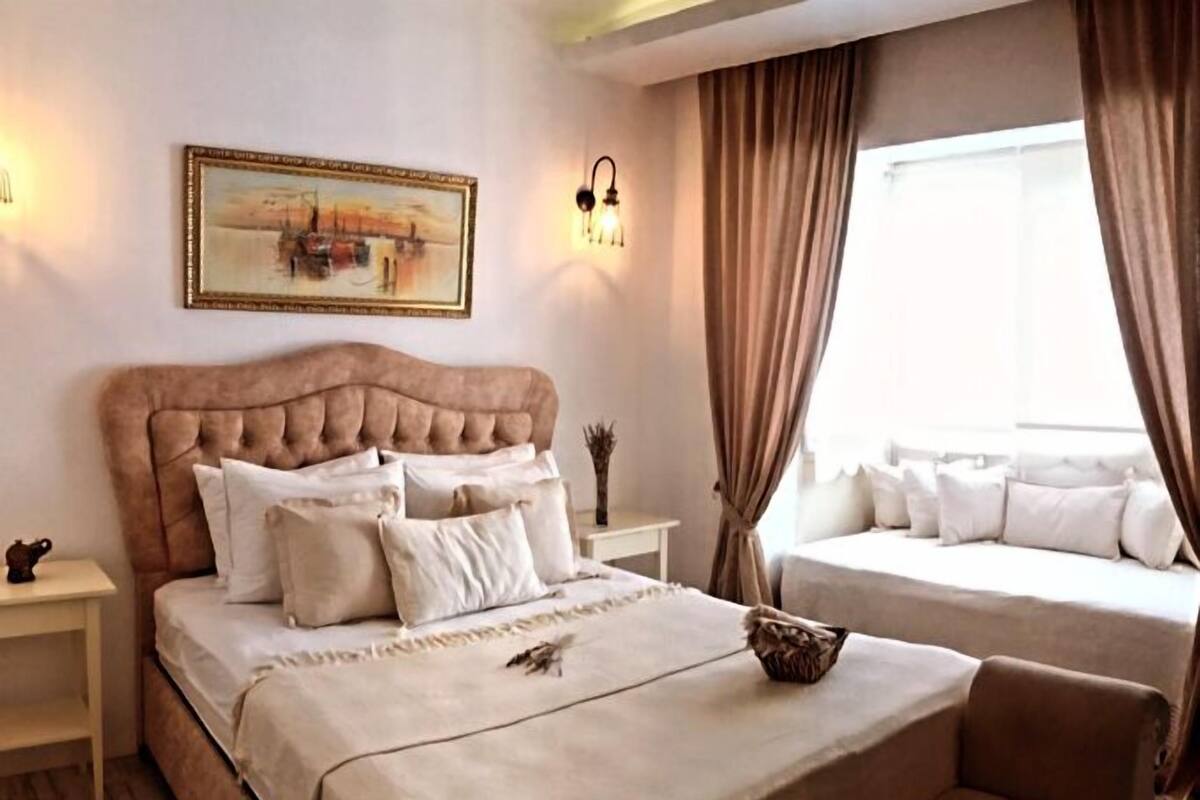 A bedroom with a large bed, a smaller bed, a chair, a nightstand, a lamp, and a painting on the wall.