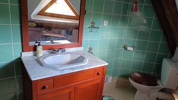 A bathroom with a sink, mirror, wooden cabinet, toilet, and green tiled walls.