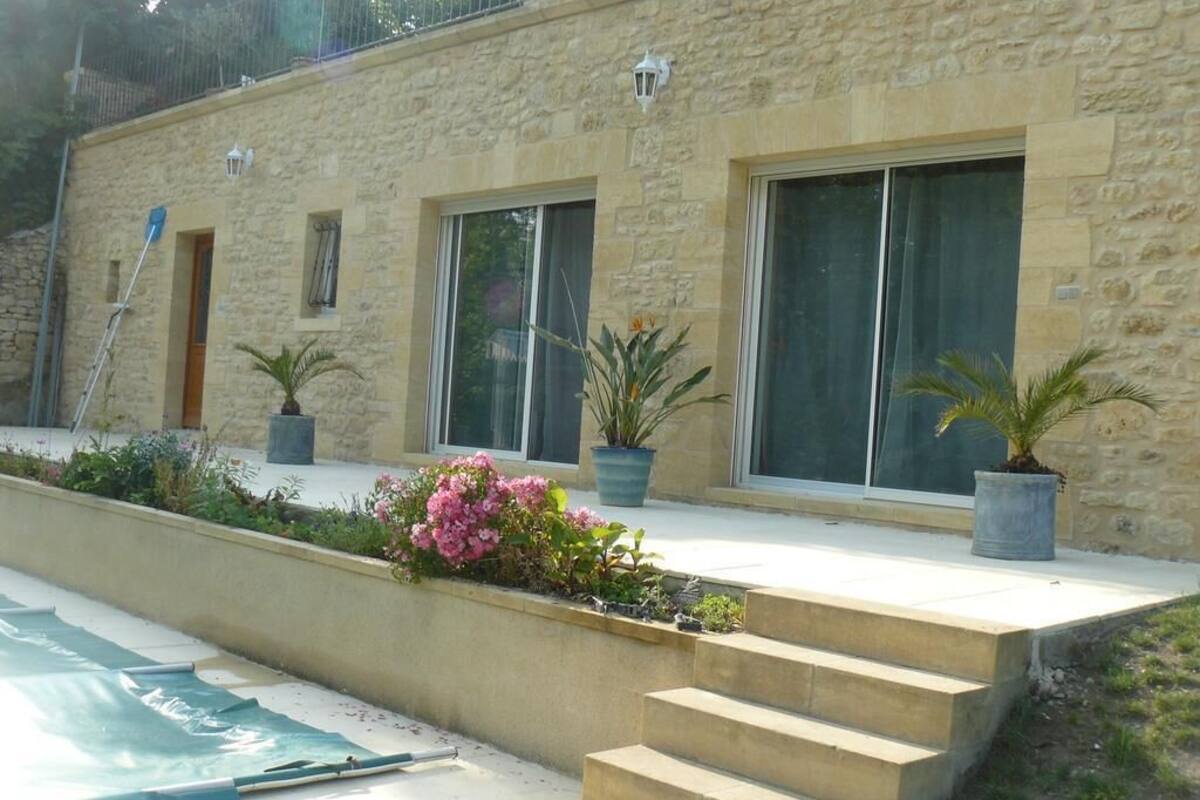 Un bâtiment en pierre doté de grandes fenêtres, d’un escalier en béton et de plantes en pot.