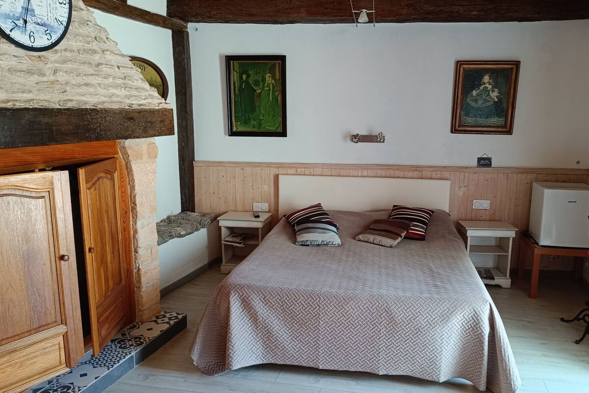 Une chambre à coucher avec un lit, une tête de lit en bois, deux tableaux, une horloge, un porte-manteau et une petite table sur laquelle se trouve un téléviseur.