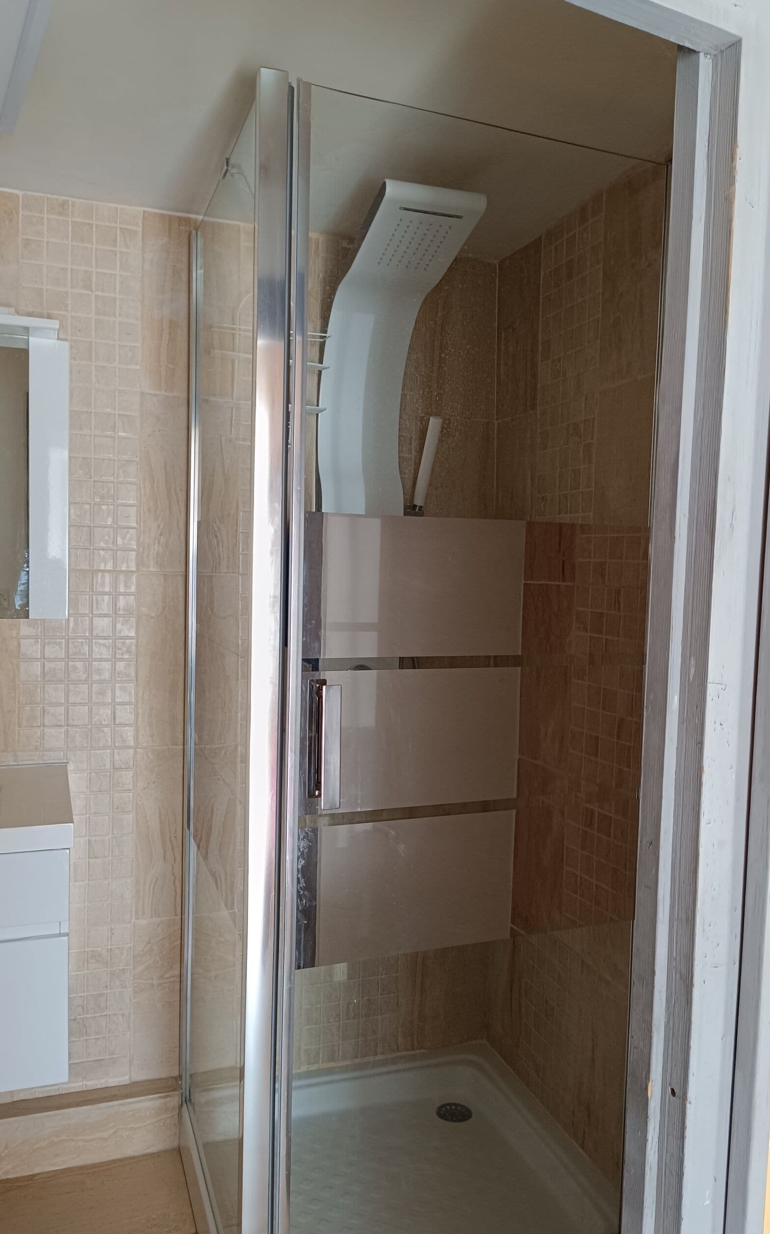Une douche avec une porte en verre, un mur carrelé et un plafond blanc.