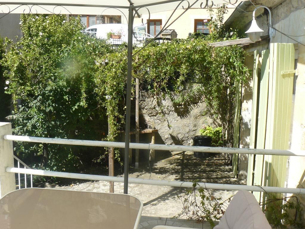 A view through a metal gate with a stone wall and greenery in the background.