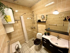 Un baño con baldosas color beige, un inodoro blanco, un lavabo, un espejo y una ducha.