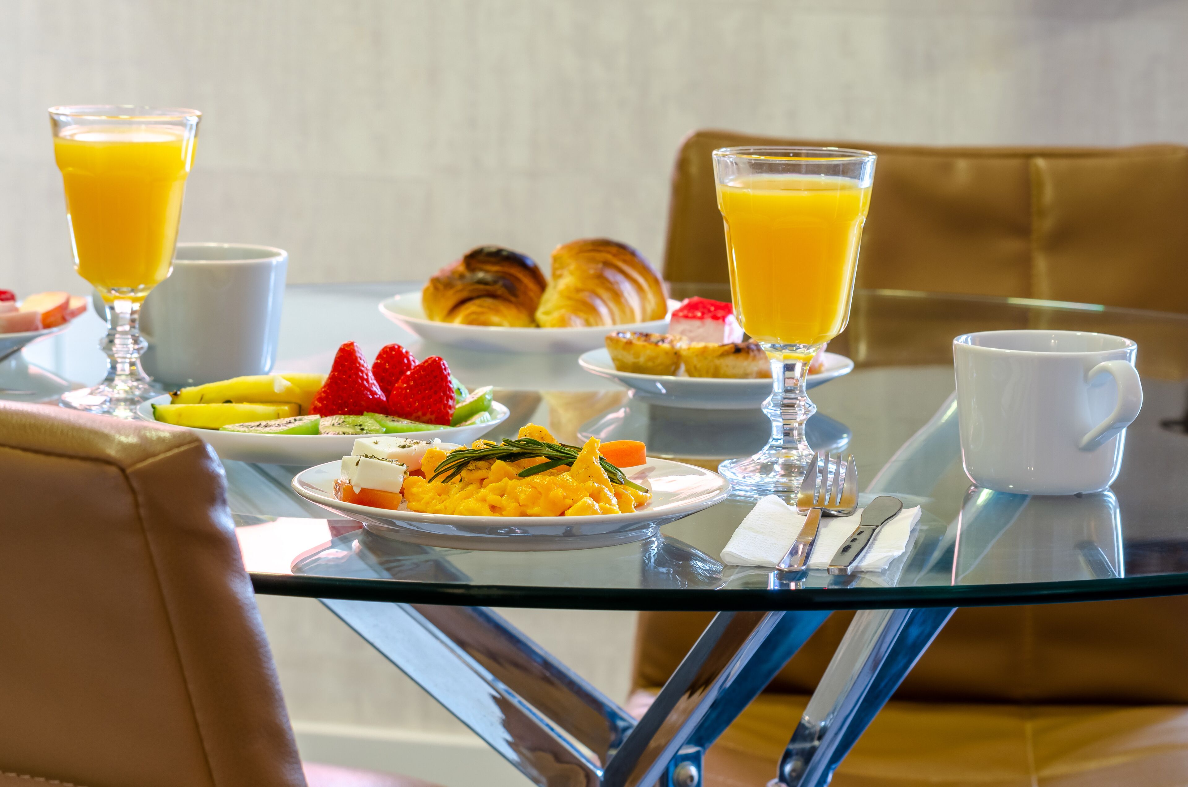 Una mesa de desayuno con cruasanes, fruta, huevos revueltos y zumo de naranja.