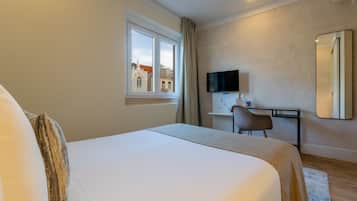 A hotel room with a large bed, a desk with a chair, a flat-screen TV, and a window with a view of buildings.