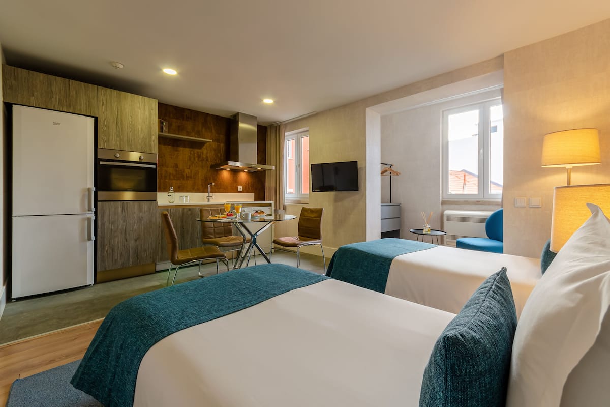A hotel room with two beds, a kitchenette, a TV, and a window.
