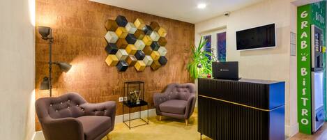 Un área de recepción moderna con pared de textura de madera, dos sillones cómodos, un mostrador de recepción negro y un letrero verde que dice 'GRAB & DISTRO'.