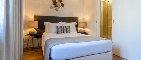 A modern bedroom with a large bed, two bedside tables with lamps, a decorative wall piece, and a wooden floor.