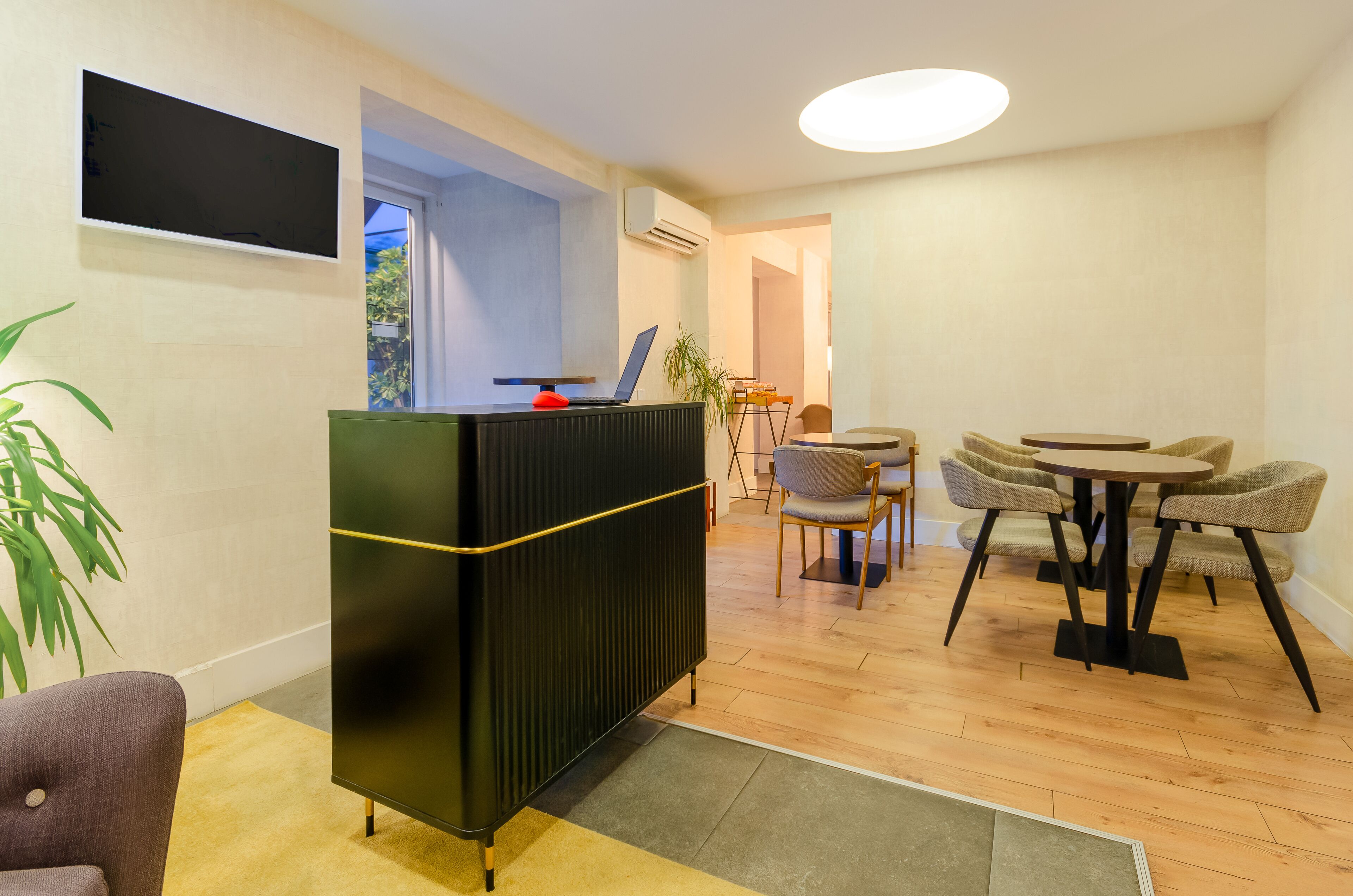 A modern living room with a black entertainment unit, a laptop, and a dining area with round tables and chairs.