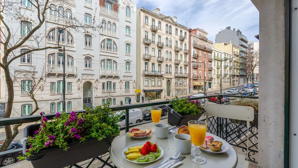 Un balcón con una mesa lista para el desayuno, que incluye un plato de fruta, un croissant y un vaso de jugo de naranja.