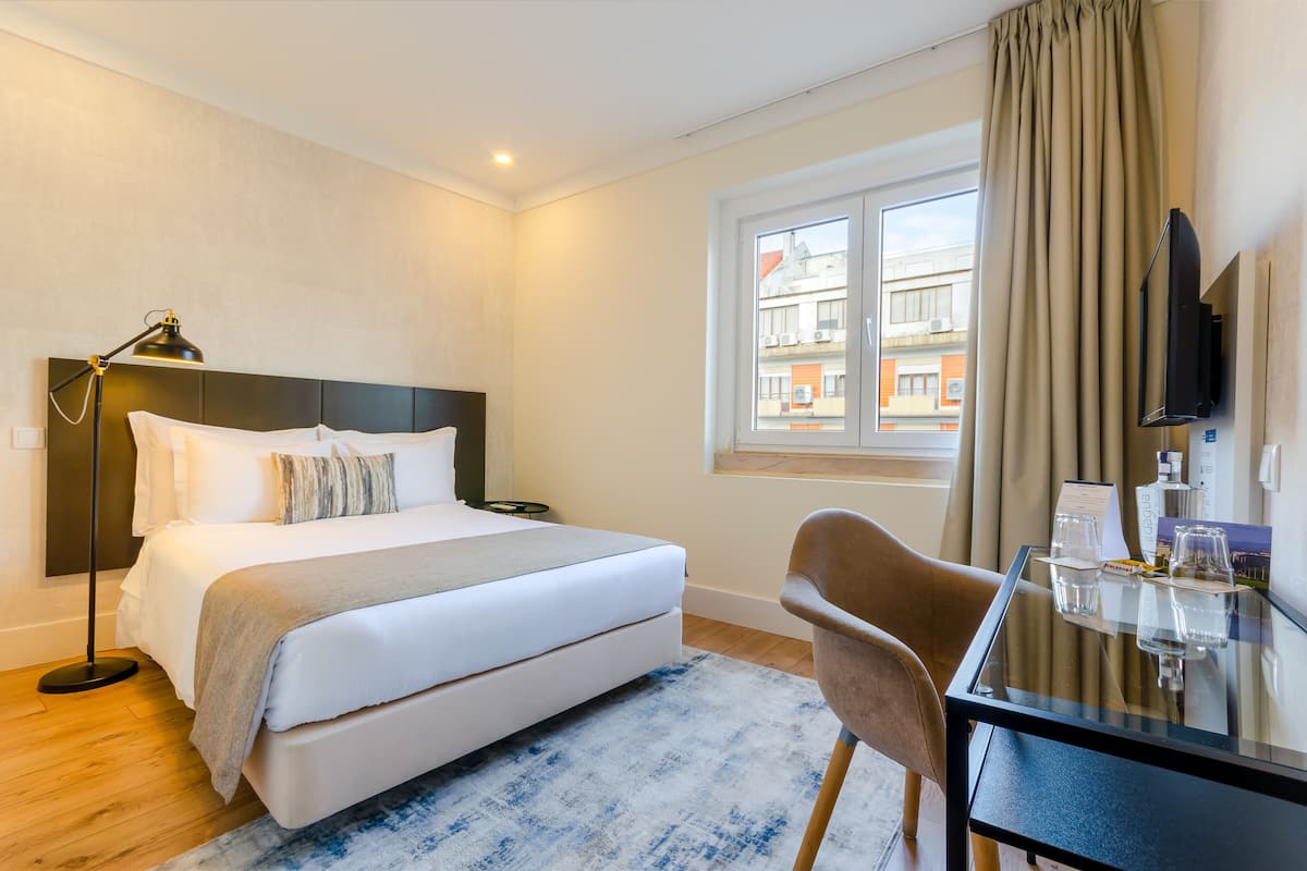 A hotel room with a bed, bedside table, chair, and a window with curtains.