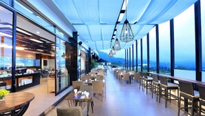 A modern restaurant with a long counter, wicker chairs, and large windows offering a view of the city. - Aston Inn Batu - Malang (Batu)