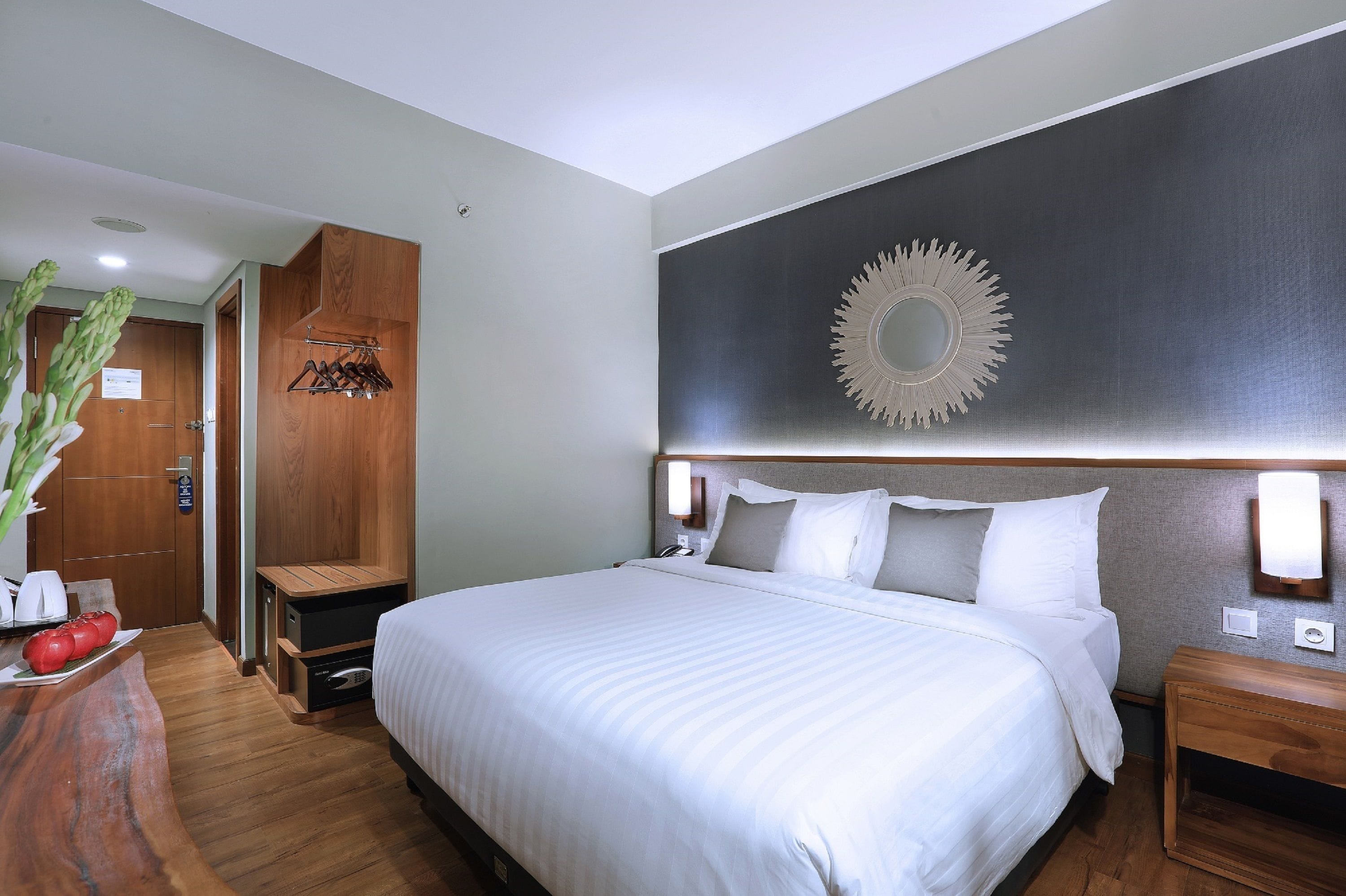 A hotel room with a large bed, wooden headboard, and a wall-mounted mirror.