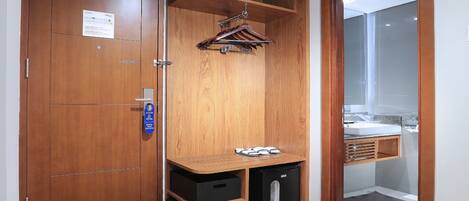 A wooden wardrobe with a hanging rack, a small black storage unit, and a door with a fire safety notice.