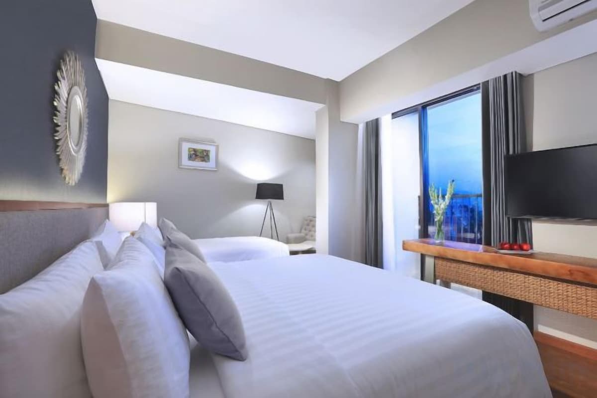 A hotel room with two beds, a TV, a window with a view, and a lamp.