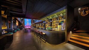 A bar area with a curved counter, bar stools, and shelves stocked with bottles. - Aston Inn Batu - Malang (Batu)