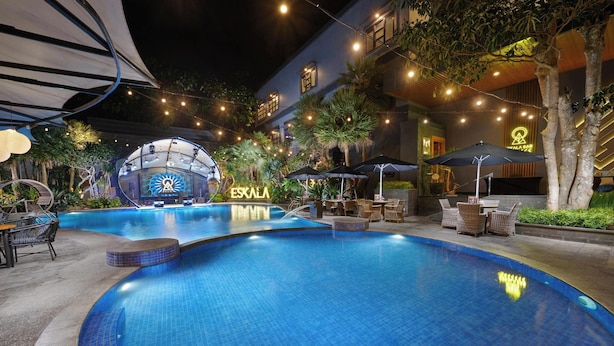 A swimming pool with lounge chairs and umbrellas, surrounded by a building with a sign reading "ESKALA". - Aston Inn Batu - Malang (Batu)