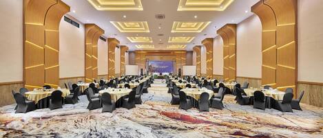 A conference room with multiple tables and chairs, a patterned carpet, and a stage at the front.