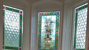 Een meerlaags interieur met drie glas-in-loodramen, een centraal decoratief raam en een klein raam met een plant.