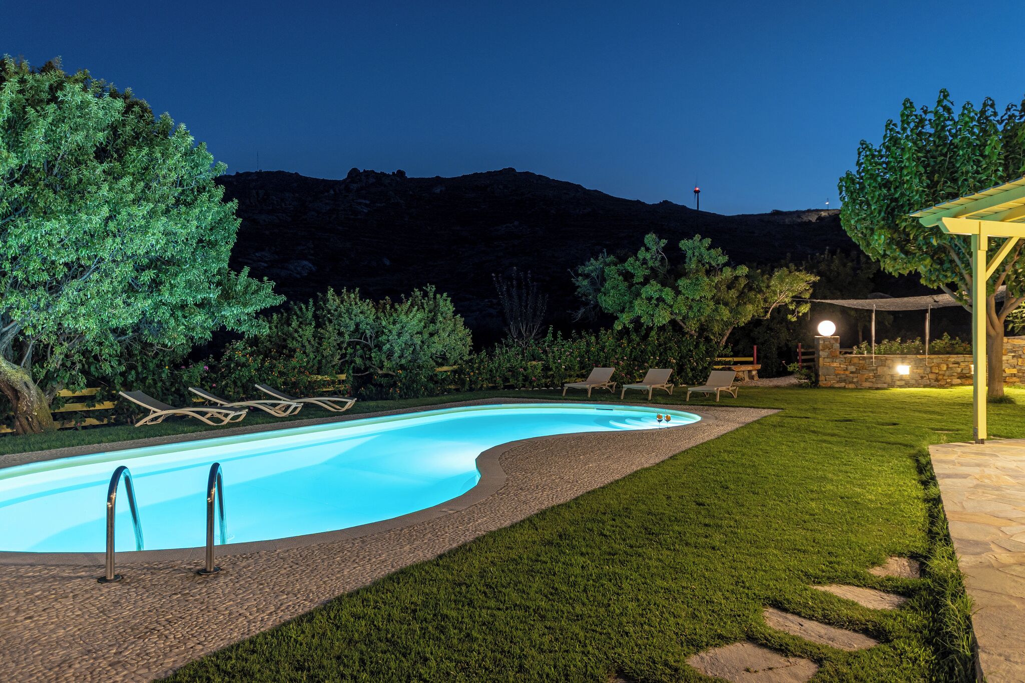 A swimming pool with lounge chairs, a stone pathway, and a mountainous backdrop.