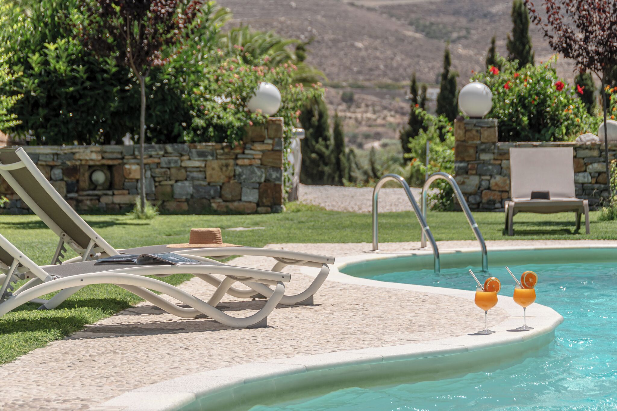 Ein Poolbereich mit Liegestühlen, einer Steinmauer und Blick auf die Landschaft.
