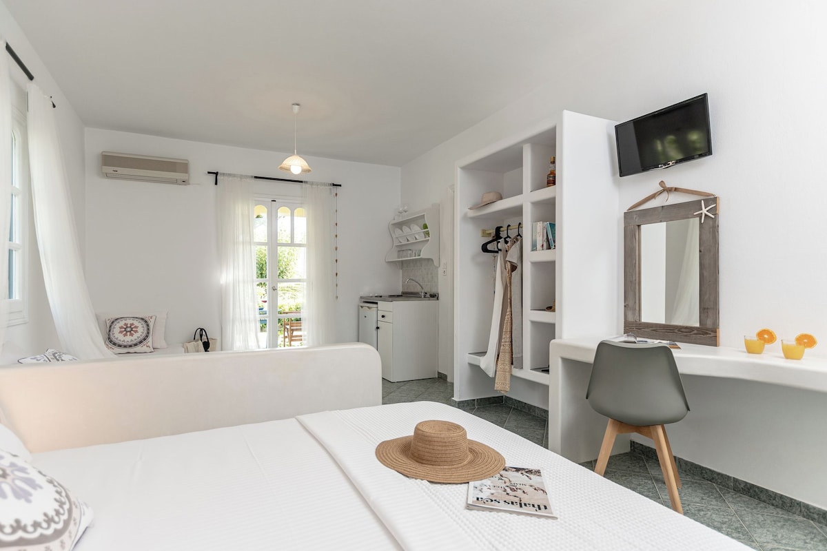 Ein Hotelzimmer mit Bett, Schreibtisch, Stuhl, Fernseher, Spiegel und einer kleinen Küchenzeile.