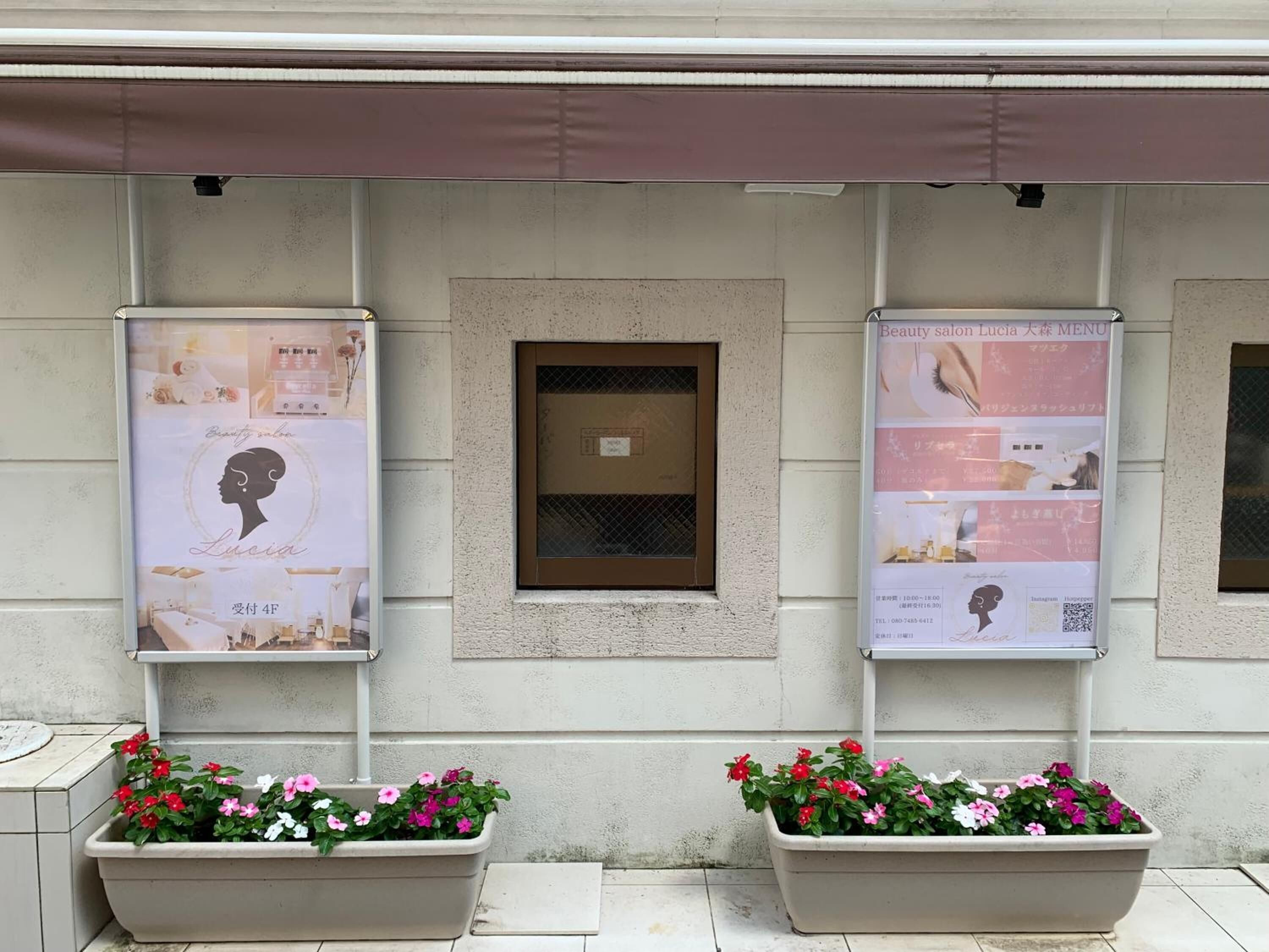 A building facade with two large posters advertising a beauty salon, a small window, and two flower planters.