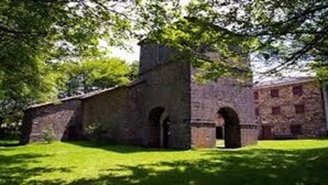 Un bâtiment historique en pierre, doté d’arcades et d’une cheminée, entouré d’une pelouse verdoyante.
