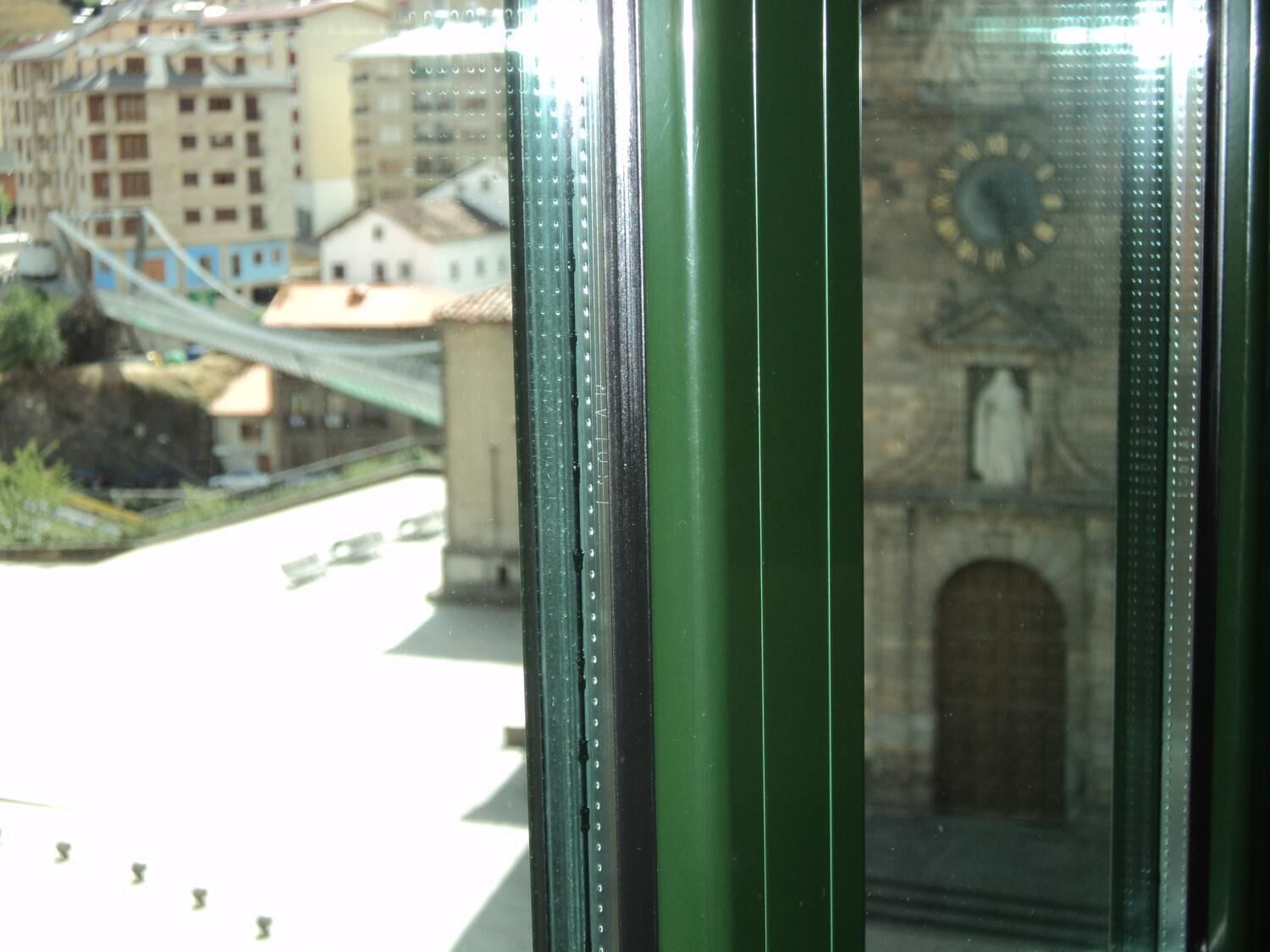 A view through a window with a green frame, featuring a clock tower and a bridge in the background.