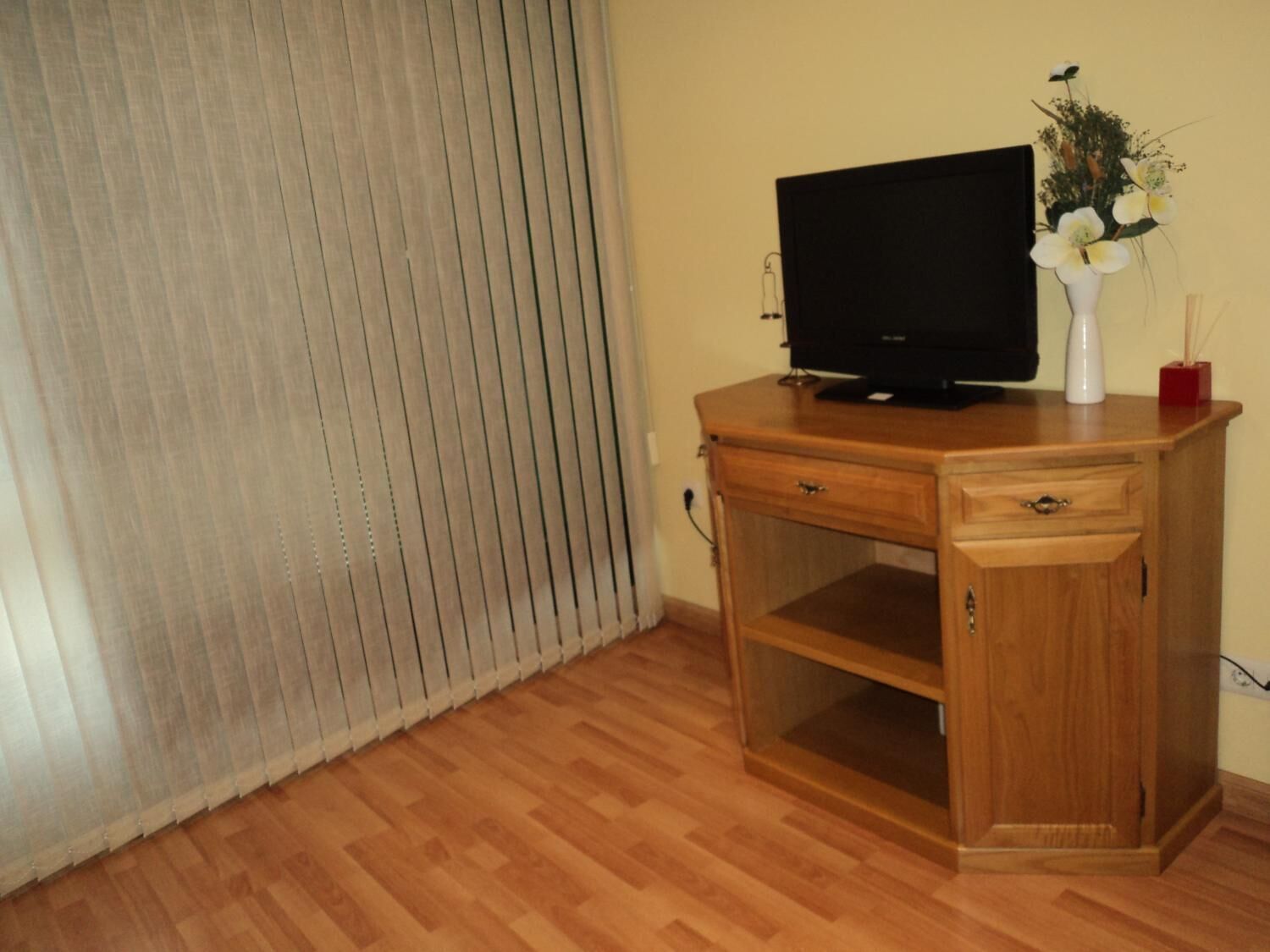A wooden desk with a television, a vase with flowers, and a red candle holder.