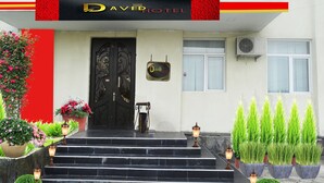 Entrada de hotel com porta preta, uma placa acima da porta e degraus que levam à entrada.