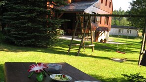 An outdoor dining setup with a picnic table, plates with food, and a swing in the background. - Kammbaude Neuhermsdorf (Hermsdorf-Erzgebirge)