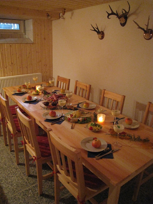 Une table de salle à manger en bois, dressée pour un repas, avec des chaises, des bougies et des bois de cerf accrochés au mur.