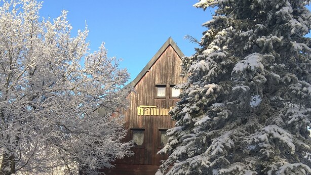 A wooden building with a sloped roof, surrounded by snow-covered trees. - Kammbaude Neuhermsdorf (Hermsdorf-Erzgebirge)