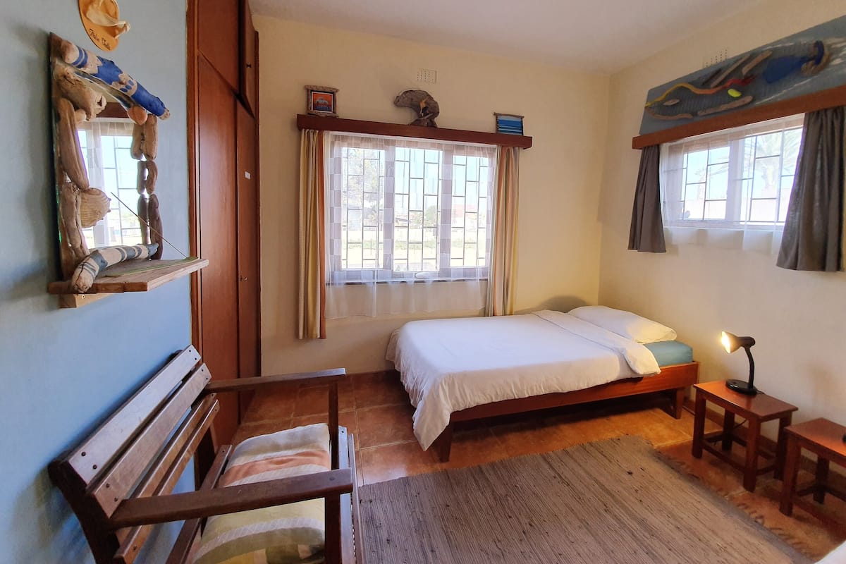 Ein Schlafzimmer mit einem Bett, einer hölzernen Bank, einem kleinen Tisch und einem Fenster mit Vorhängen.