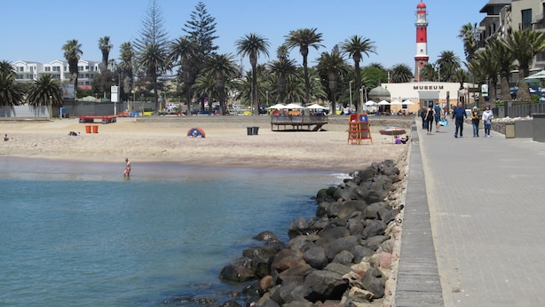 Una playa con costa rocosa, palmeras y un faro.