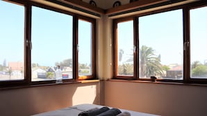 Habitación de hotel con cama, ventana que ofrece vistas a palmeras y edificios, y una toalla sobre la cama.