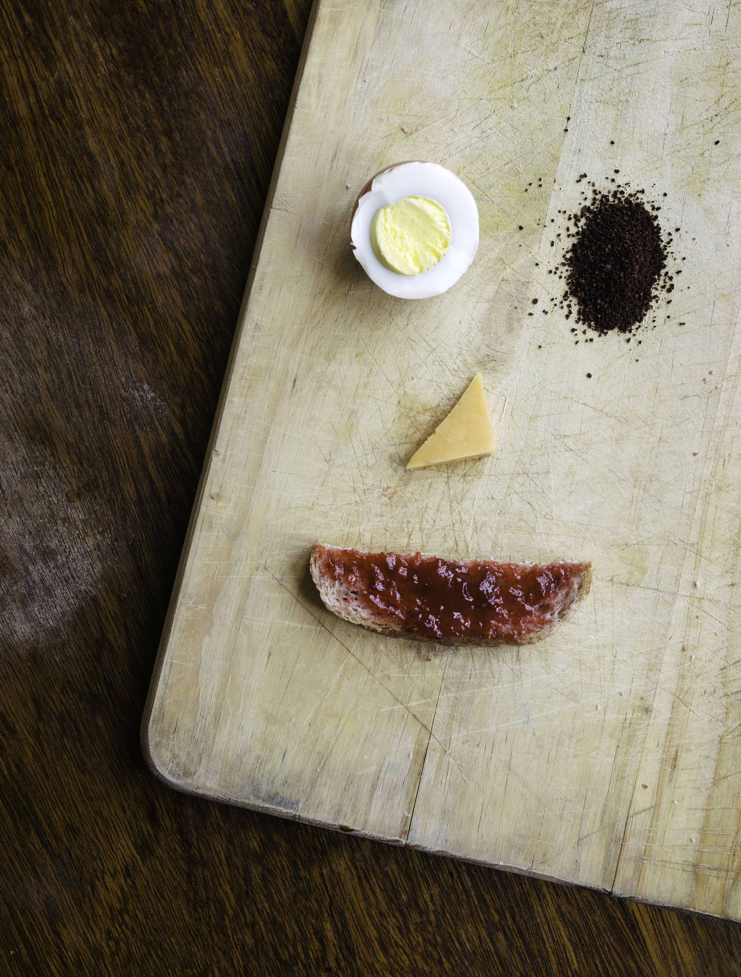 Une planche à découper en bois sur laquelle on a posé un morceau de viande, une tranche de fromage, un petit bol de beurre et un tas de poivre.