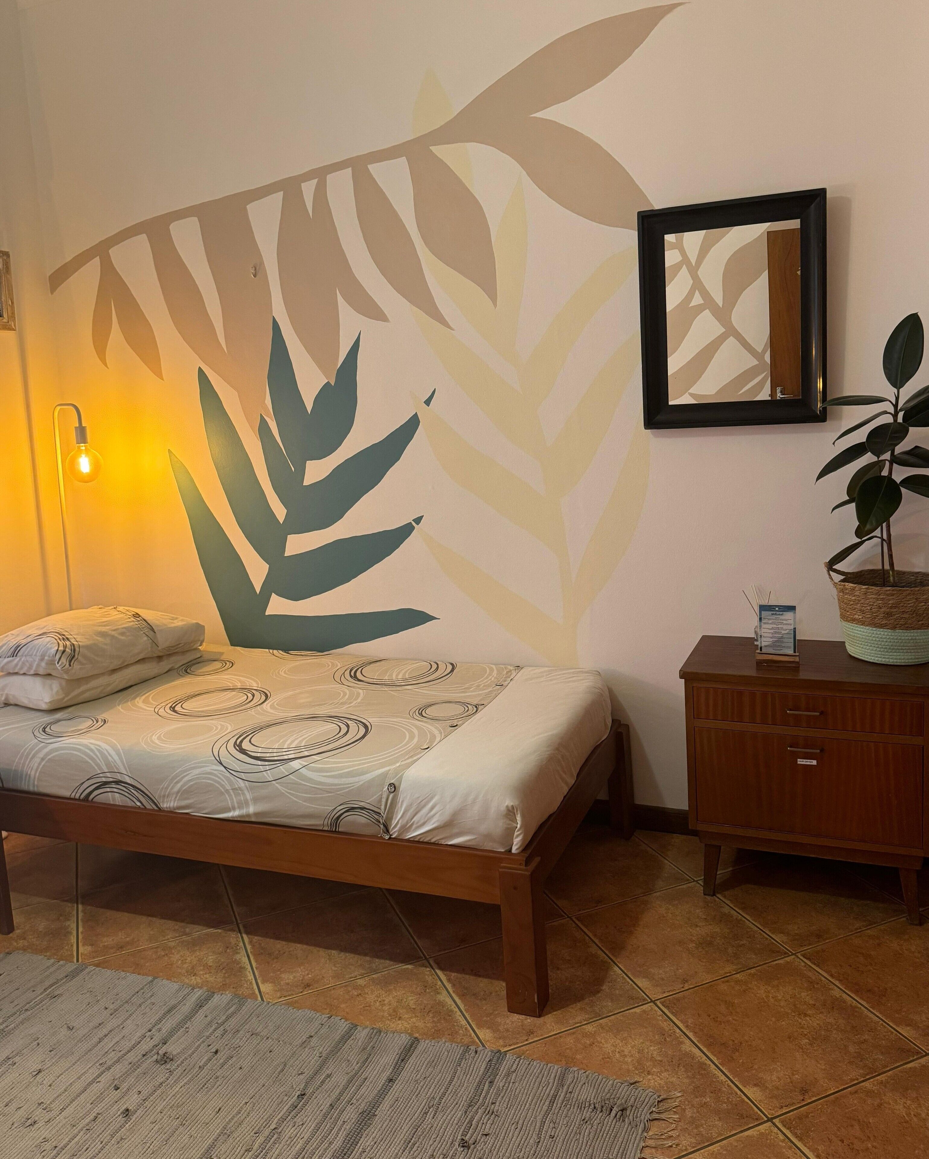 A bedroom with a bed, a nightstand, a lamp, and a wall with a leaf pattern.